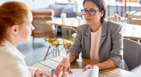 Completion of successful negotiations: confident middle-aged entrepreneur passing contract for signature to her business partner while they sitting at cozy coffeehouse